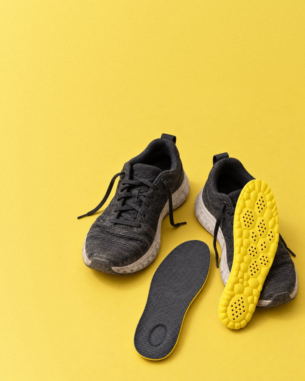 Getragene schwarze Arbeits-Sneaker auf Gelb, davor zwei STUNDE NEUN Einlegesohlen: eine mit der Stoffseite nach oben, eine mit der gelben Wabenseite